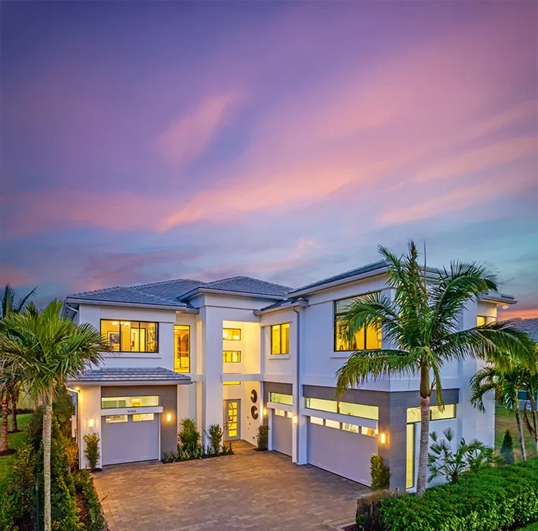 A modern luxury new construction home exterior in Palm Beach has a two story white paint with dark roof and gray trim, with tall palm trees.