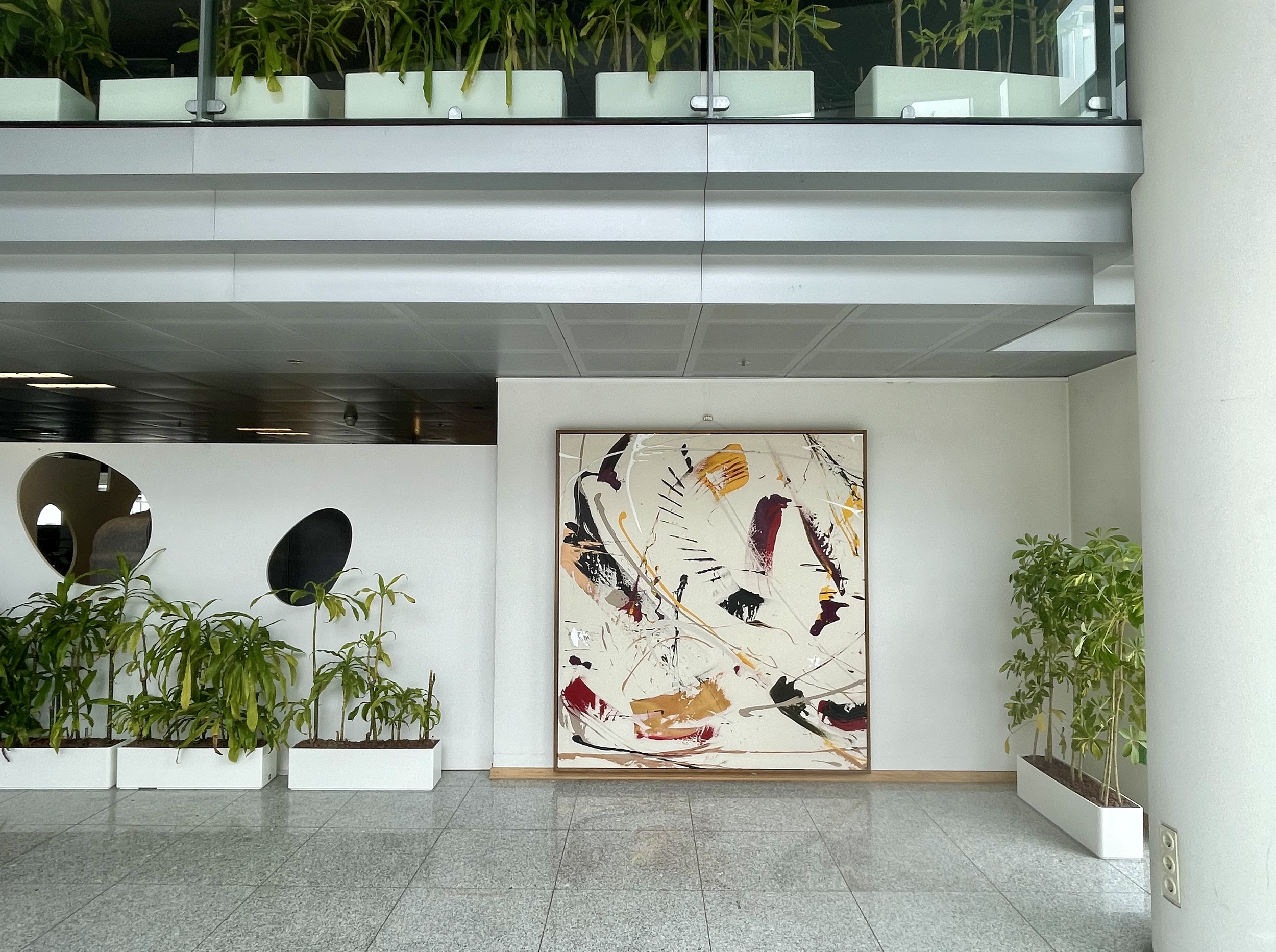 Modern cafe interior with large abstract painting on white wall, polished floor, and potted greenery