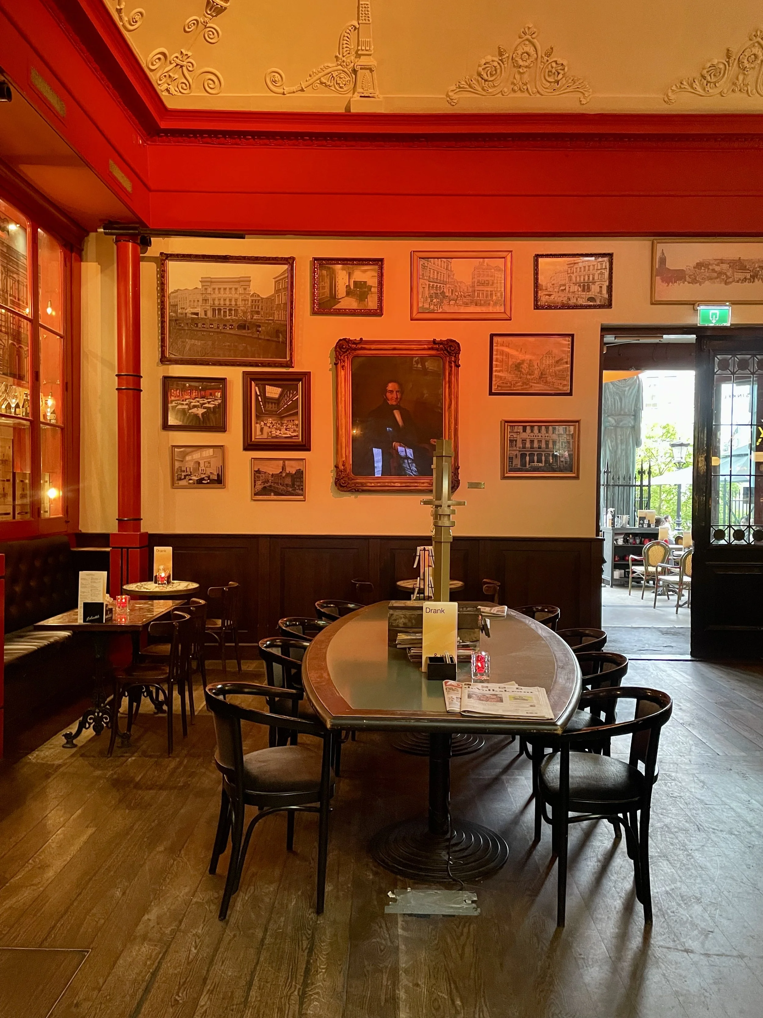 An interior shot of the Winkel van Sinkel in Utrecht shows the red cinnabar walls, white classical plaster and a gallery wall of art above a sitting area.