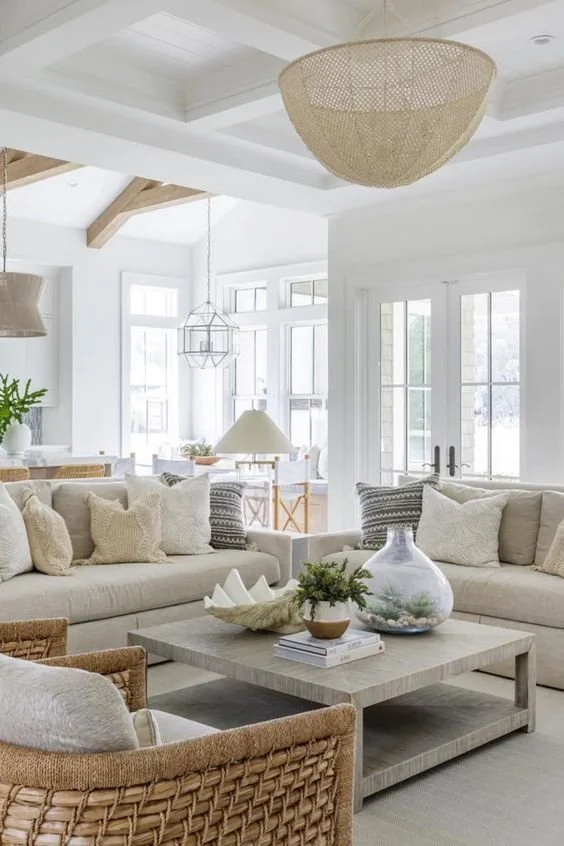 A bright and airy Palm Beach coastal living room with vintage-inspired design elements, featuring neutral-toned sofas accented with textured throw pillows, woven armchairs,