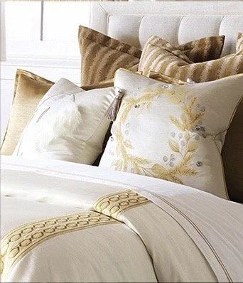 This white channel upholstered bed shows well with luxury bedding trimmed with golden tan embroidery and plush pillows.
