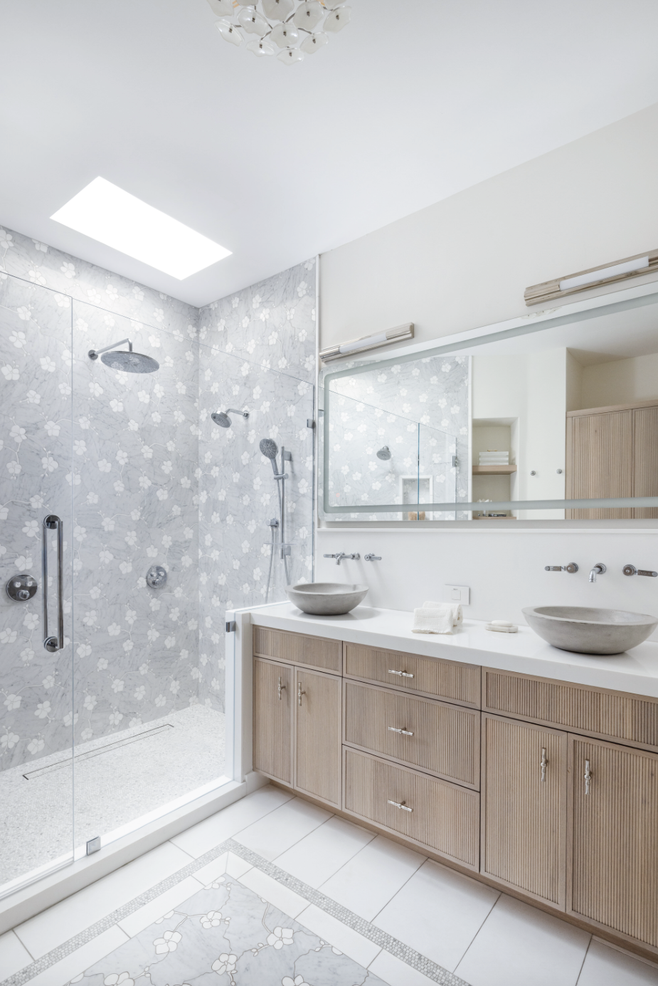 This Palm Beach bathroom of bespoke marble orchid floral pattern on walls and floors combines with custom oak reeded cabinetry, concrete vessel sinks, luxury plumbing, and layered lighting for a timeless modern aesthetic.
