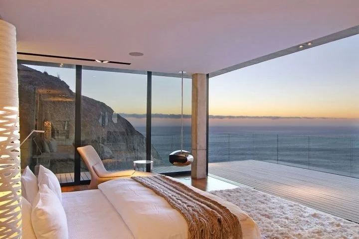 Oceanfront wellness bedroom in a luxury home with floor-to-ceiling glass and sunset views