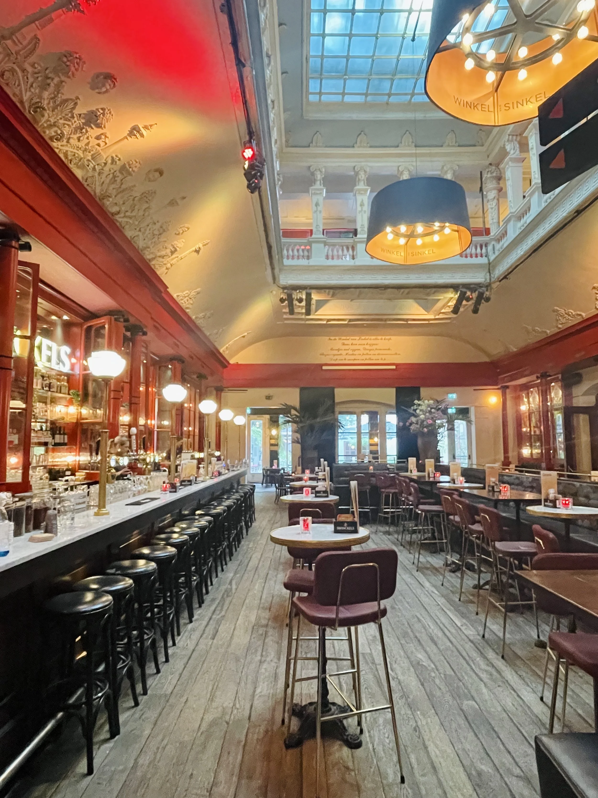 The impressive interior at Winkel van Sinkel, with its cinnabar walls, elaborate plaster, and large black chandeliers in this neoclassical, preserved building.