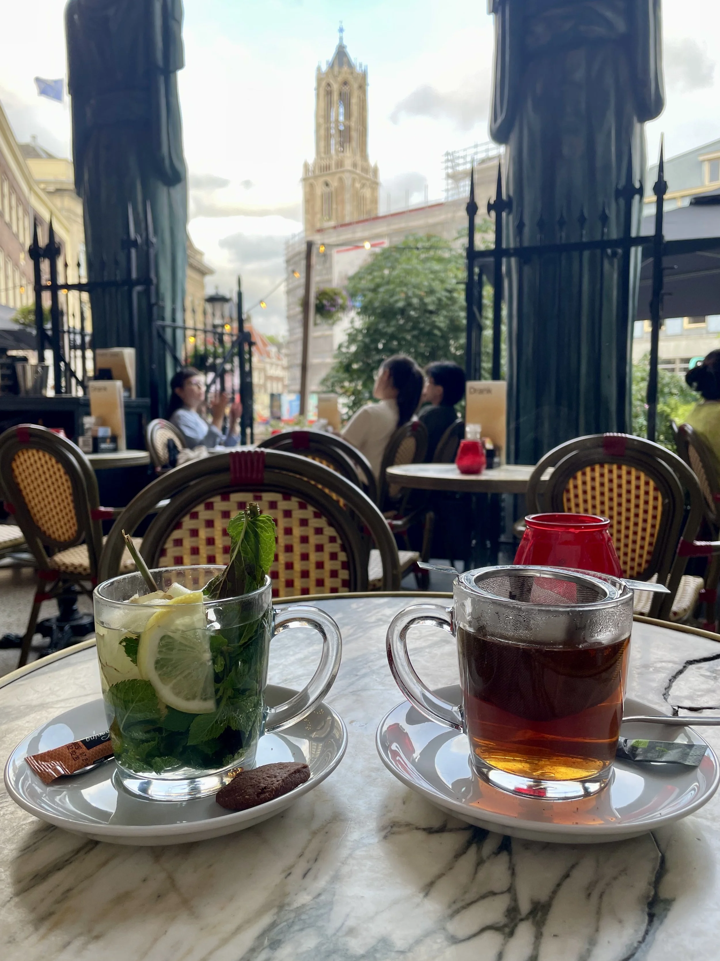 Tea for two at Utrecht's Winkle van Sinkel outdoor cafe, sitting at a marble topped bistro table with rattan bistro chairs, taking in the Utrecht quintessential view of the Dom Tower .