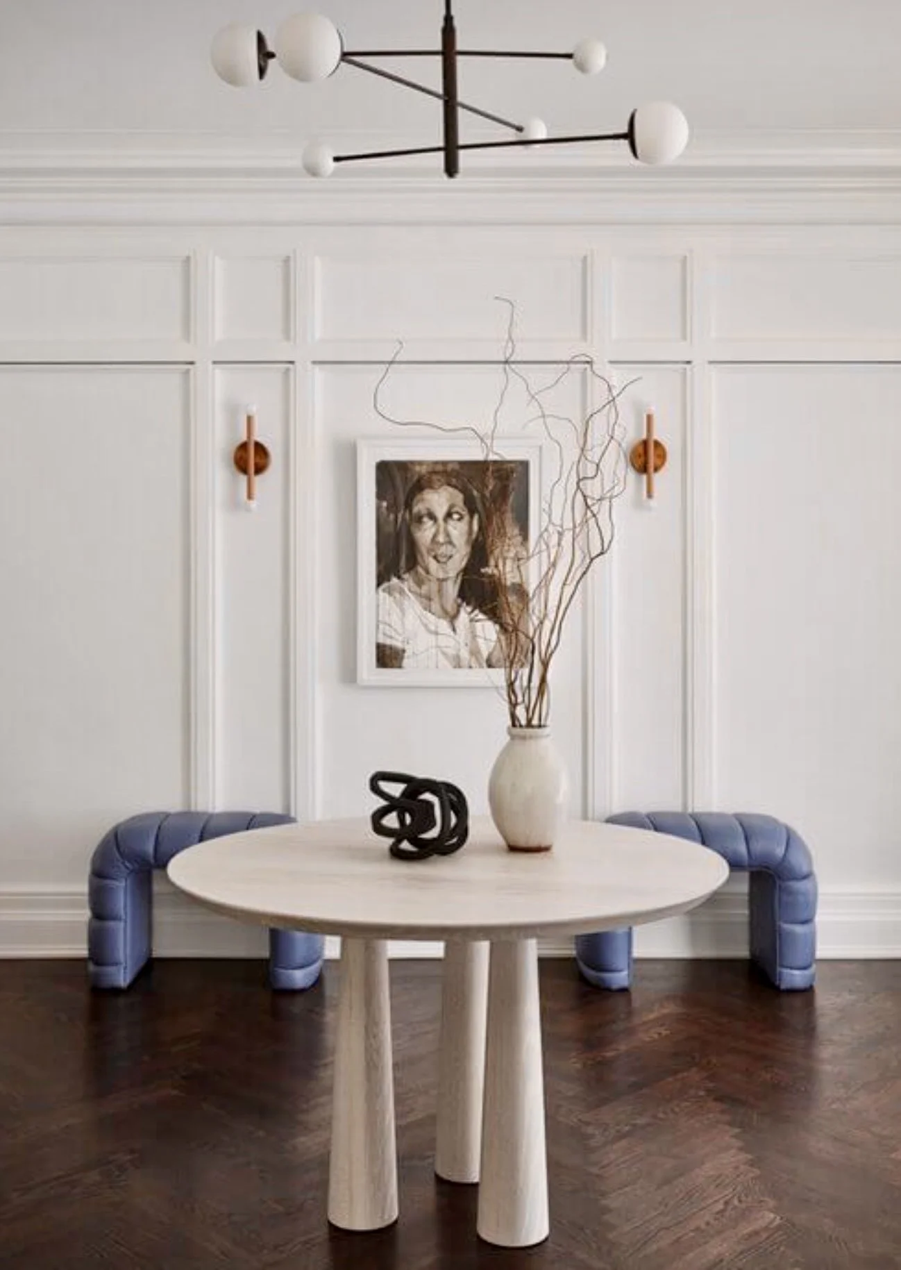 White entry has paneled walls, and a simple yet dramatic oak entry table graced by a minimalist black chandelier with round white frosted glass globes.