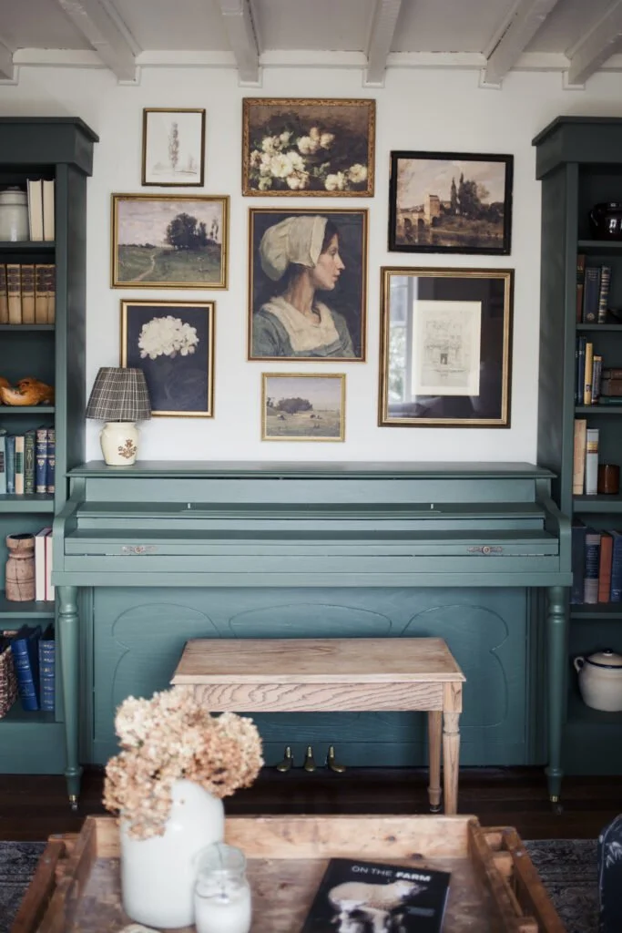 A cozy Palm Beach coastal vintage-inspired music nook featuring a muted teal upright piano framed by matching built-in bookshelves, with a natural wood bench,
