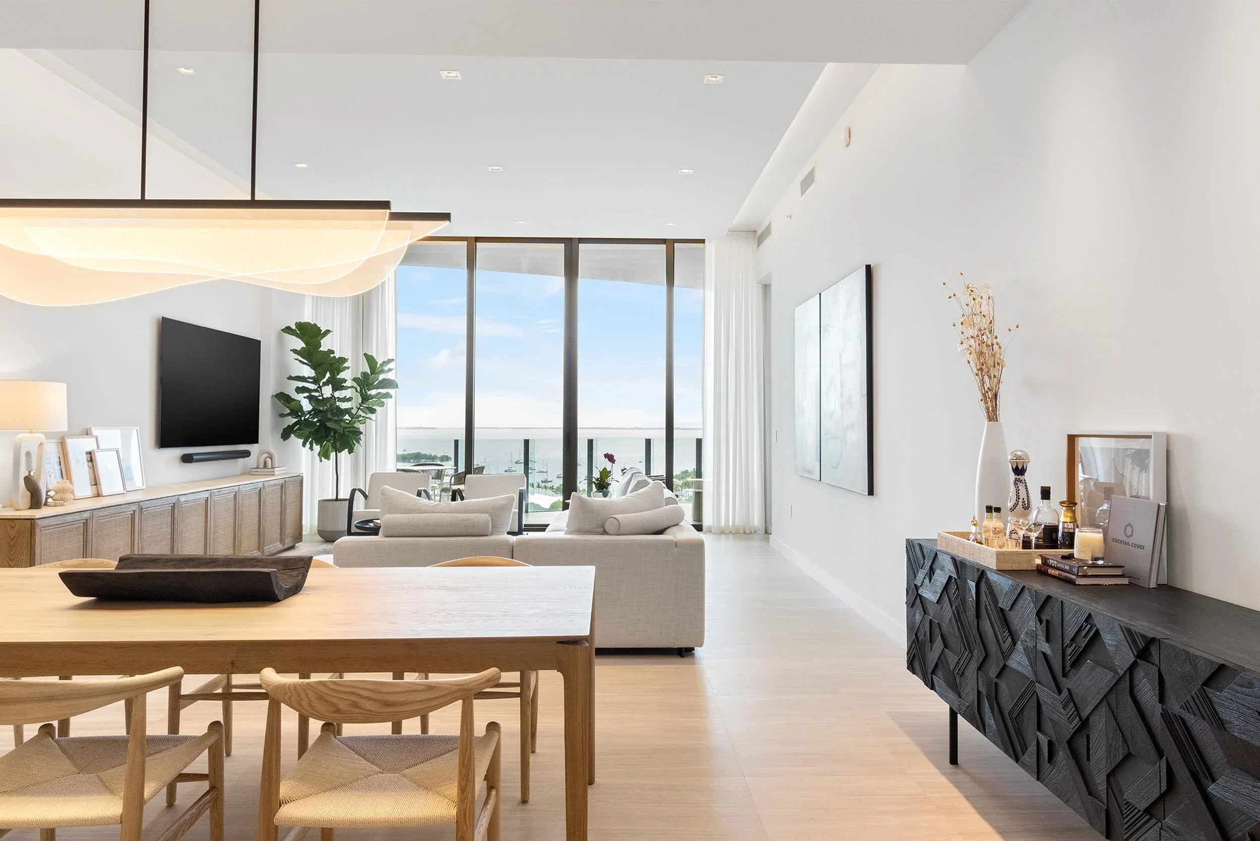 Modern coastal open living dining great room decorated warm neutrals, with water view.