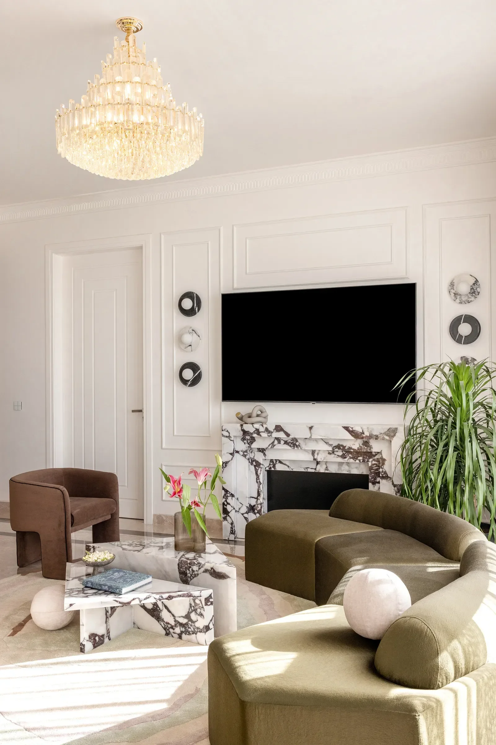 European-inspired Palm Beach living room with crystal chandelier, white paneled walls, marble fireplace, curved green sofa, modern armchair, and marble coffee table