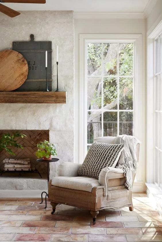 Tall windows in this European-inspired reading nook with a 12 light window, upholstered chair, marble clad fireplace, and natural daylight from two angles brighten this corner.