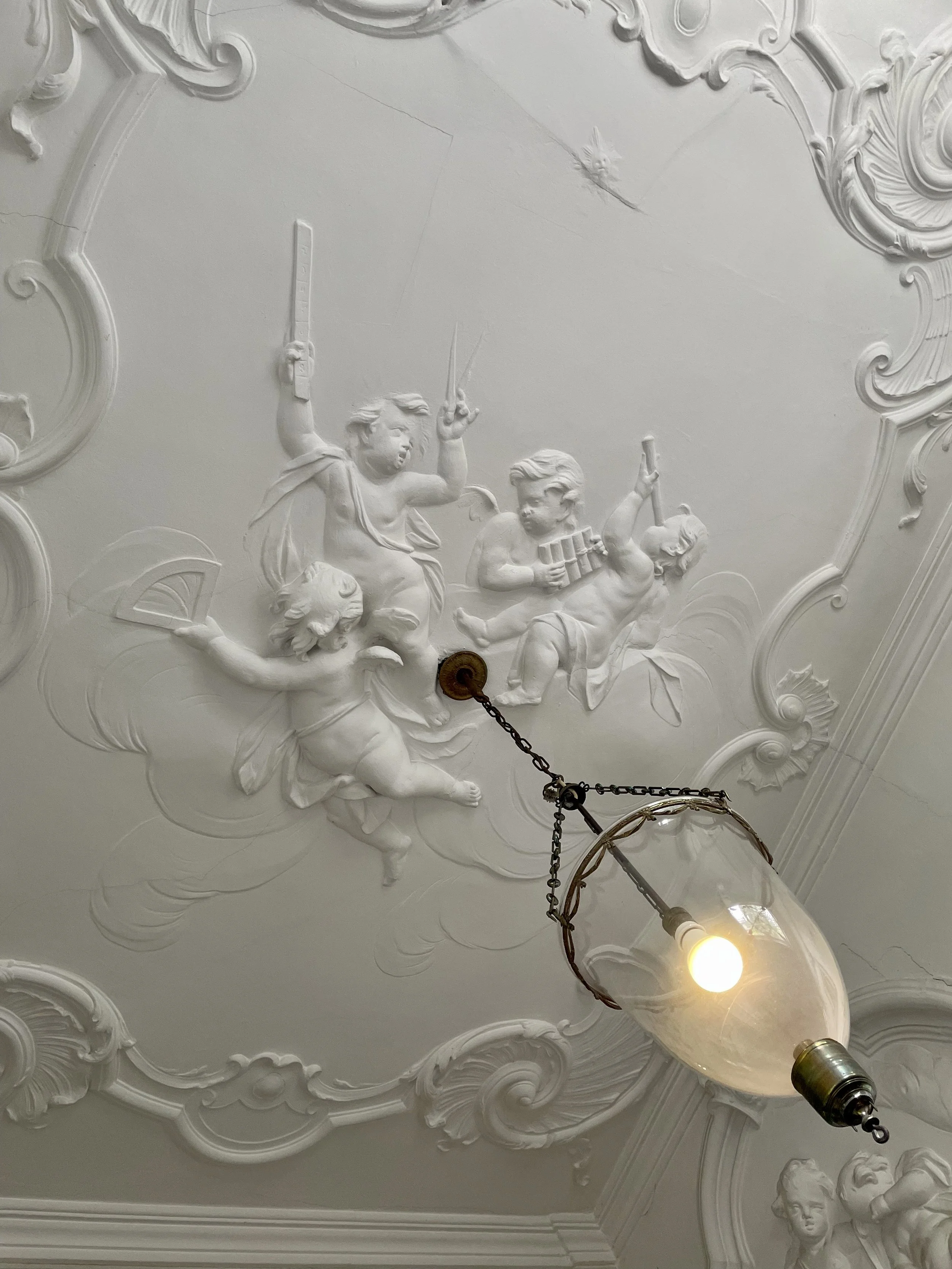 Gilded hanging lantern with intricate white plaster ceiling detailing in historic European interior