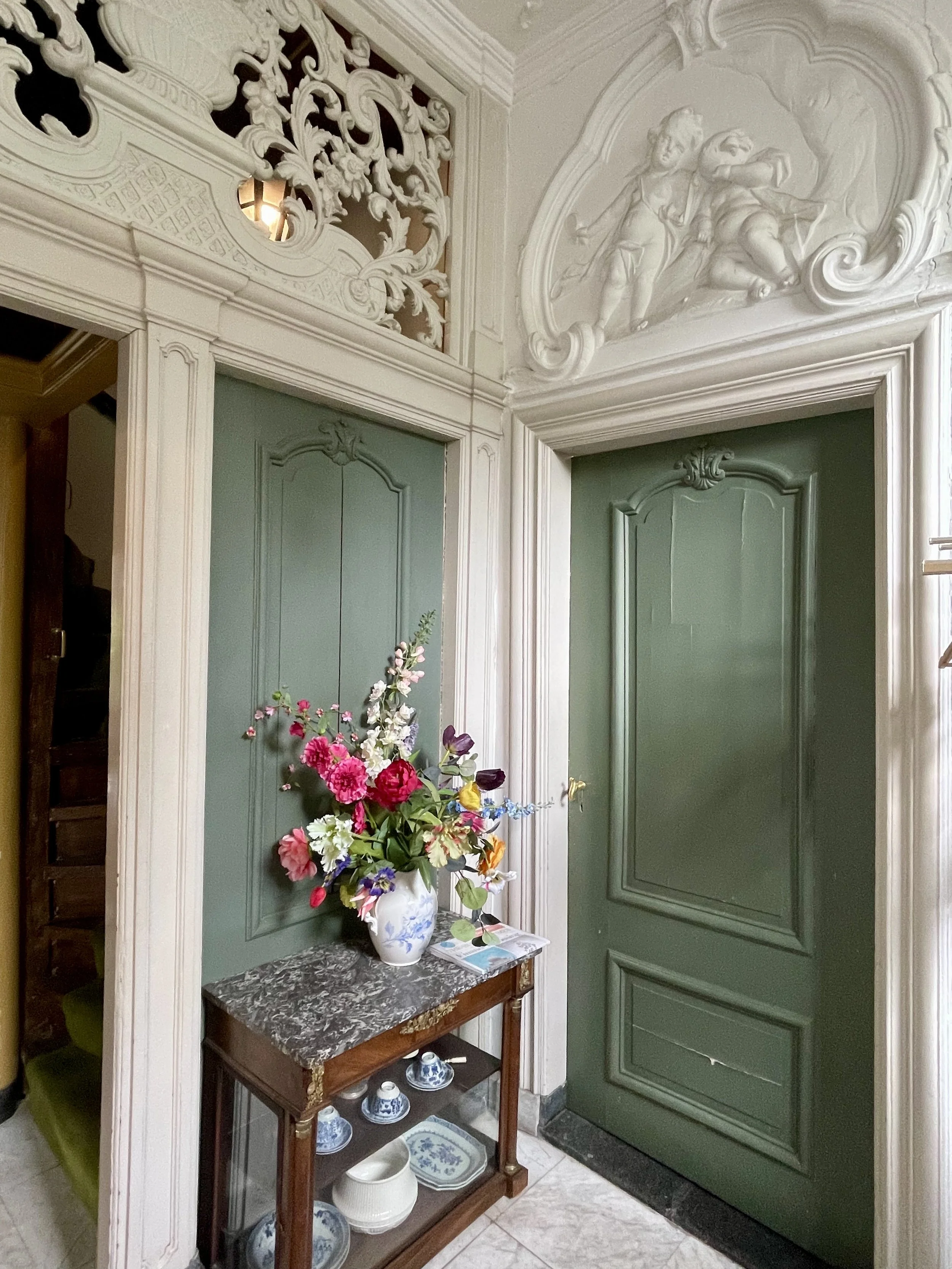 Historic Dutch foyer with sage doors, decorative plaster, and floral arrangement on a console.