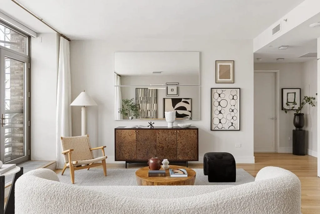 Modern Palm Beach warm minimal living room with curved white sofa, wood credenza, large mirror, and contemporary artwork.
