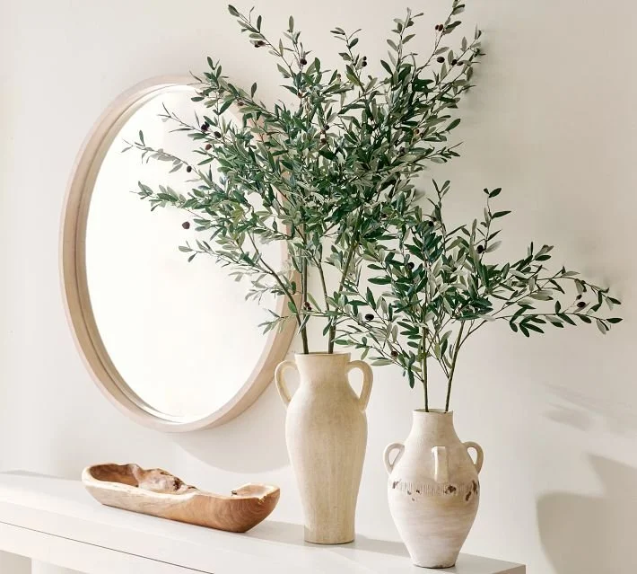 Olive branches arranged in a ceramic vessel in a refined interior.