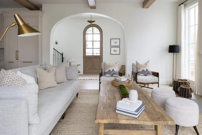Light-filled European-inspired living room with an arched doorway, linen sofa, wood beams, and neutral decor