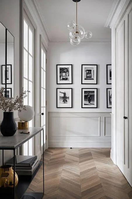 European-inspired hallway shows how light enters, with tall windows, paneled walls, chevron wood flooring, framed art, and natural daylight combine for aesthetic.