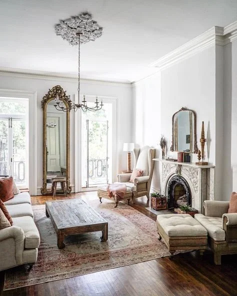 A vintage-inspired living room with Palm Beach coastal influences, featuring elegant cream armchairs, a tufted chaise lounge, a distressed wood coffee table,