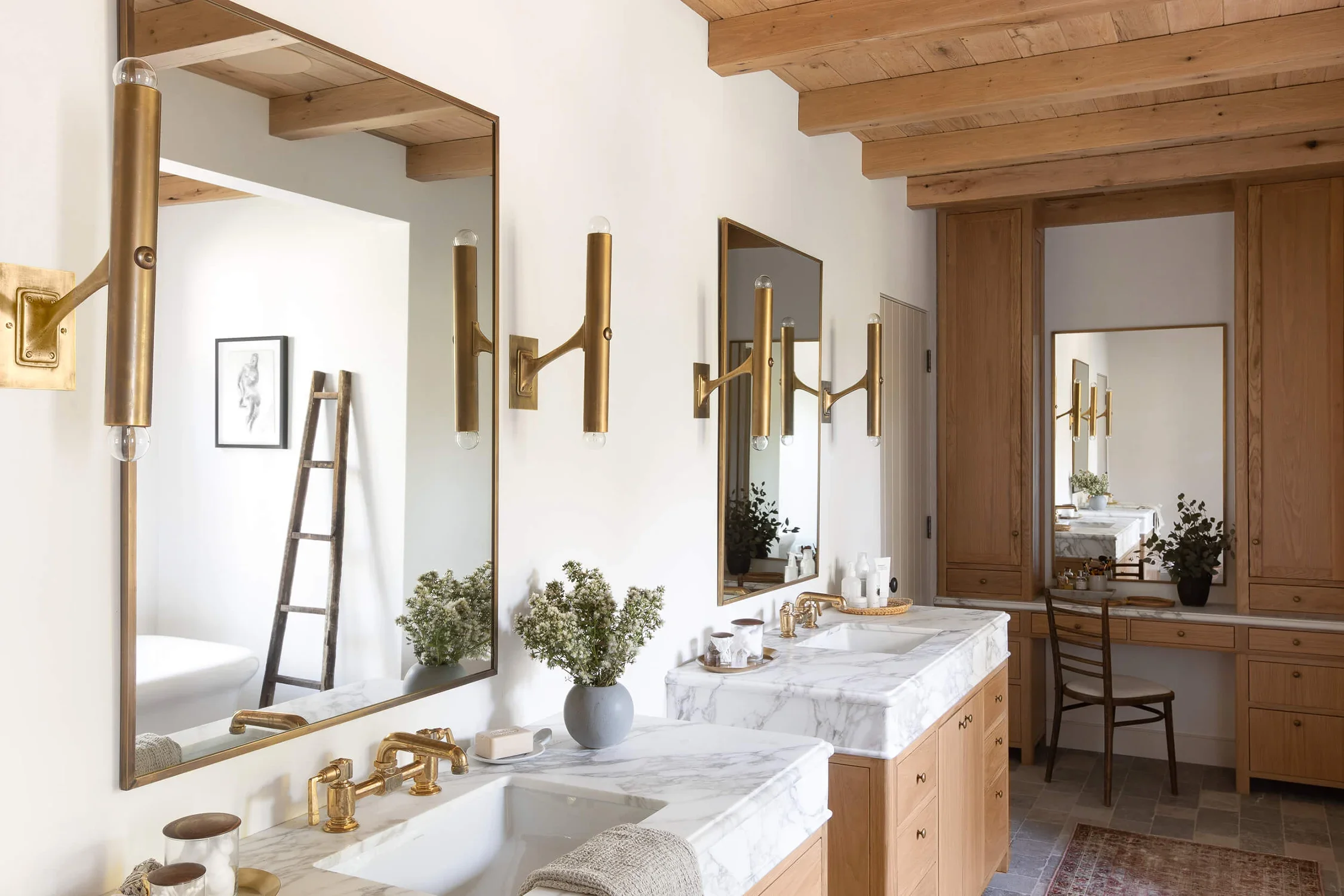Palm Beach modern bathroom with marble countertops, wood cabinetry, brass mirrors and sconces, and wood ceiling beams.