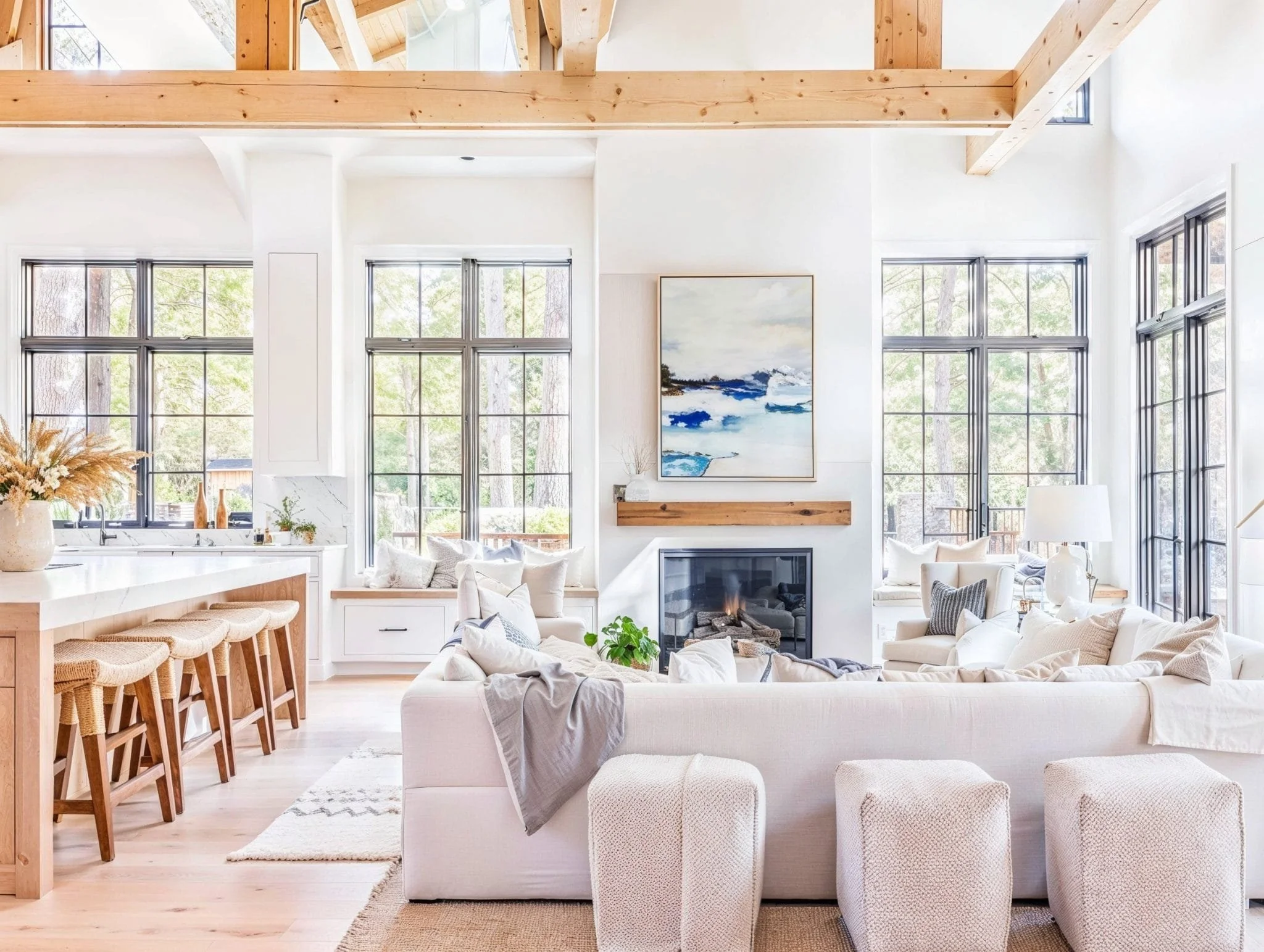 A spacious Palm Beach coastal living room with vintage design influences, featuring large black-framed windows, exposed light wood ceiling beams, an inviting white sectional sofa