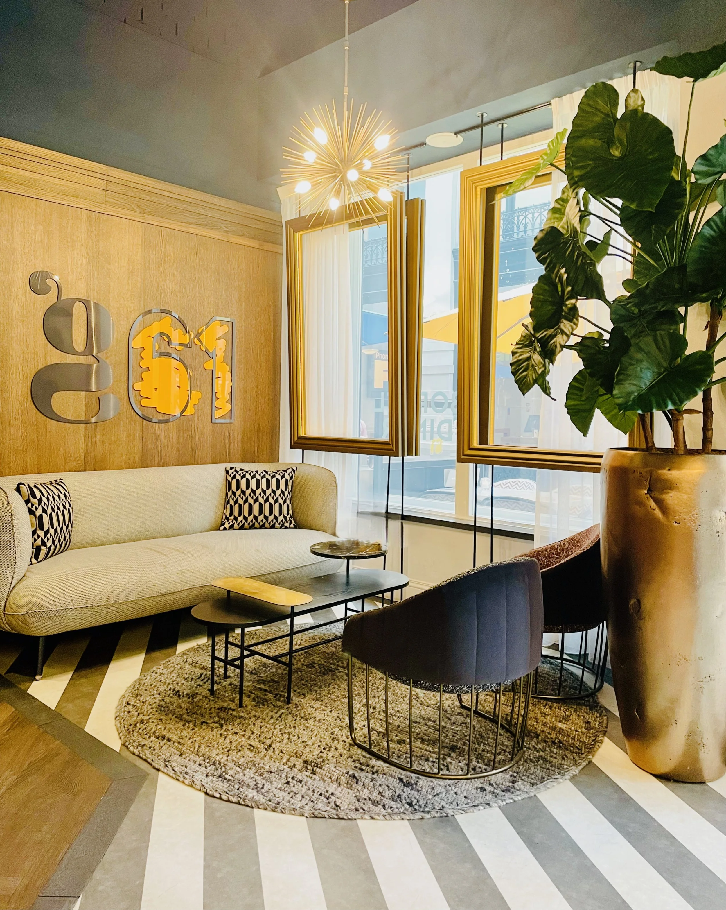 Cozy modern sitting area with wood-paneled wall, sofa, sculptural chairs, gold lighting, and large planter