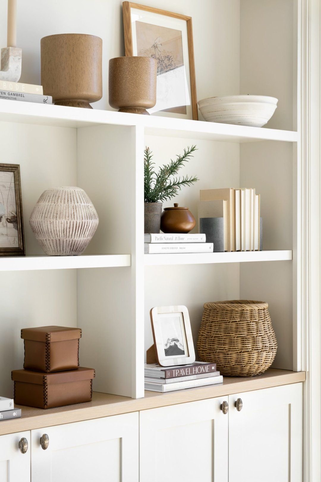 Minimal white built-in shelves feature neutral pottery, framed art, baskets, and stacked books for a warm, modern organic look. Arched white built-in bookcase with blue wallpaper and neatly arranged books, ceramics, coral, and plants.