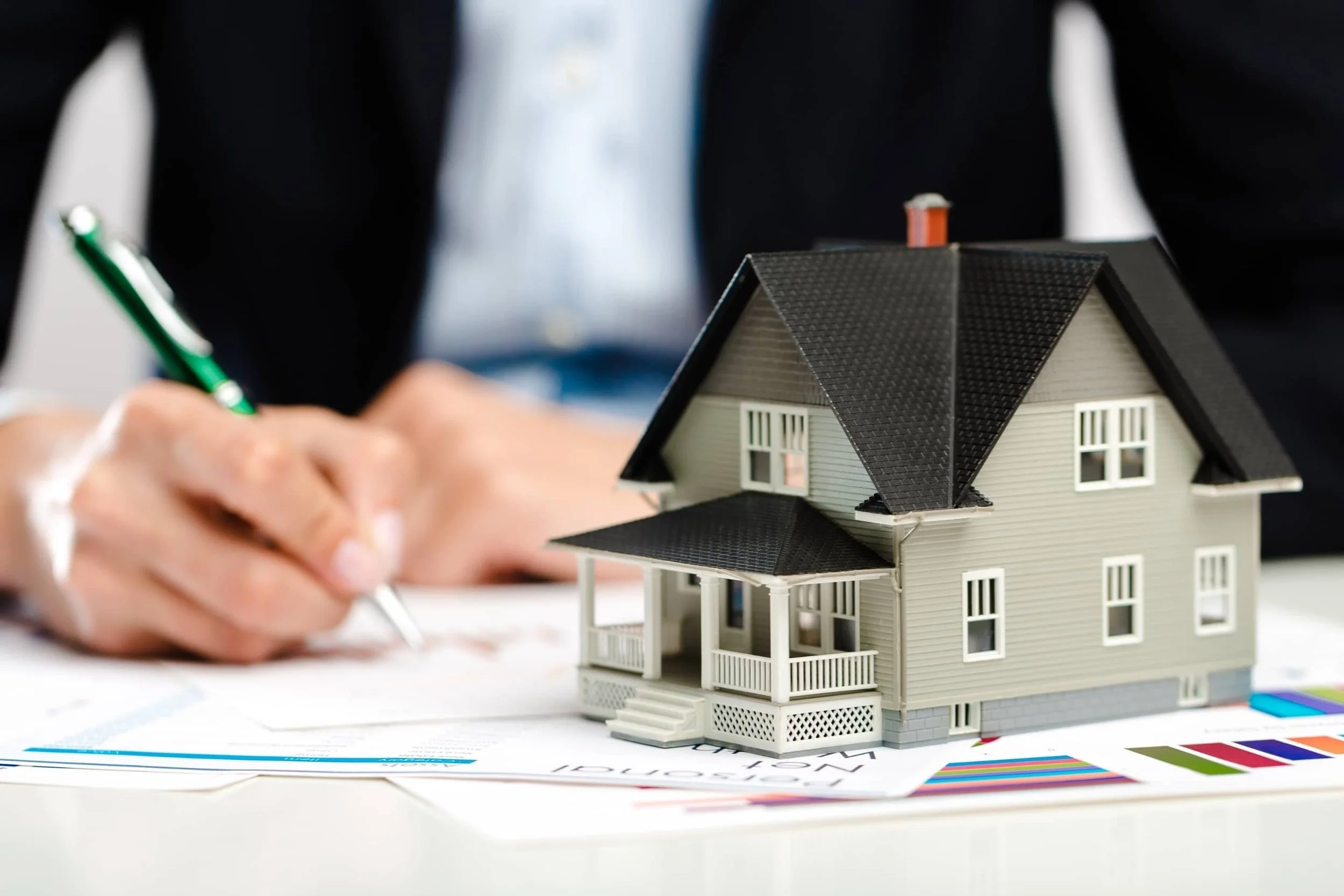 Homebuyer signing paperwork beside model house without real estate agent