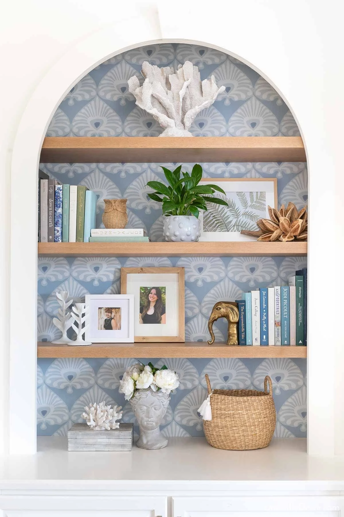 Arched white built-in bookcase with a blue and white design shows tropical blue wallpaper.