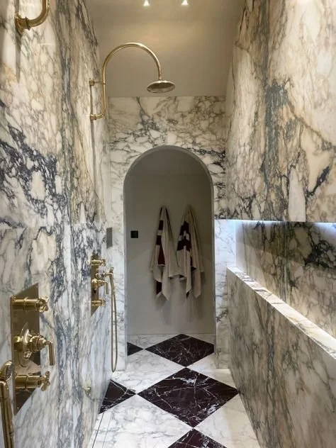 Luxurious Palm Beach marble walk‑through shower with brass fixtures and arched doorway.