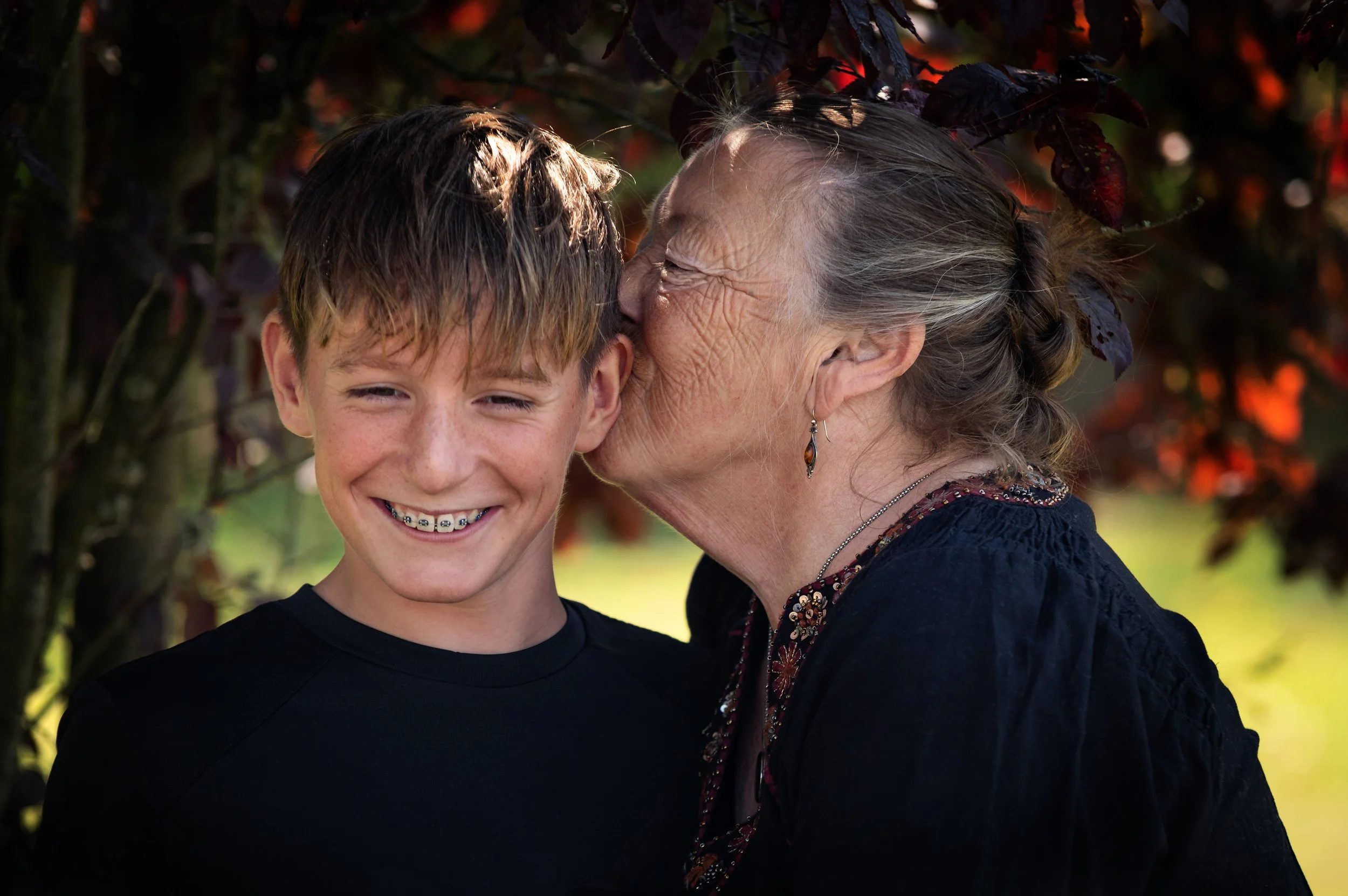 grandmother kisses her teenage grandson on the head while he giggles 