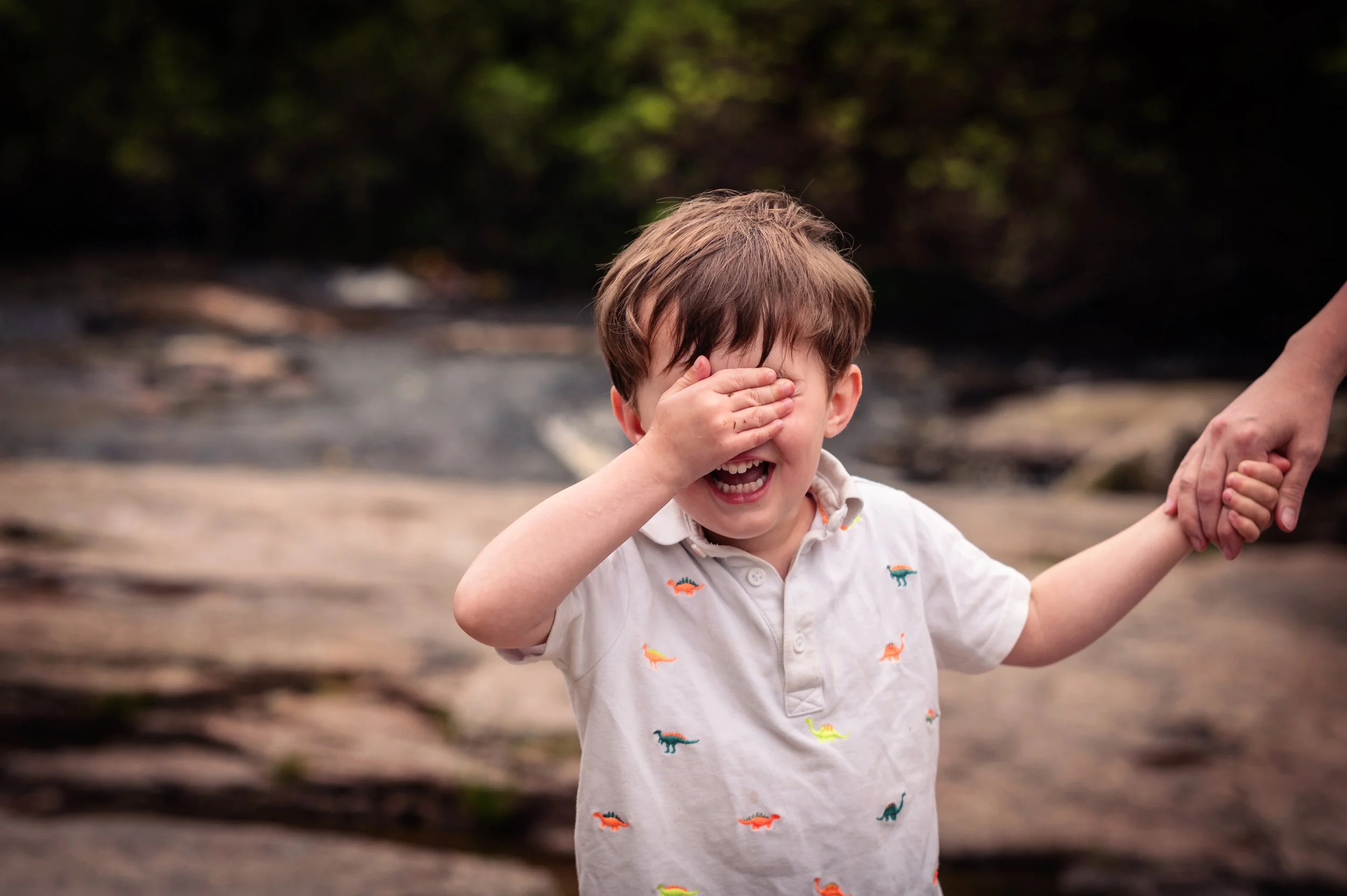 Little boy covers his eyes with one hand whilst holding his mother's hand with the other. 