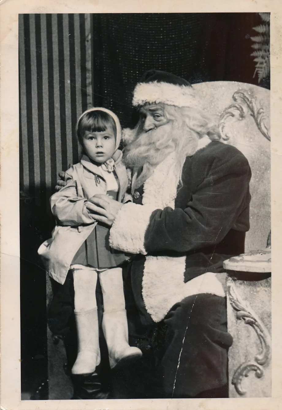 (Image: A young girl in winter hat and coat with white leotards and white boots sitting on Santa's lap.)