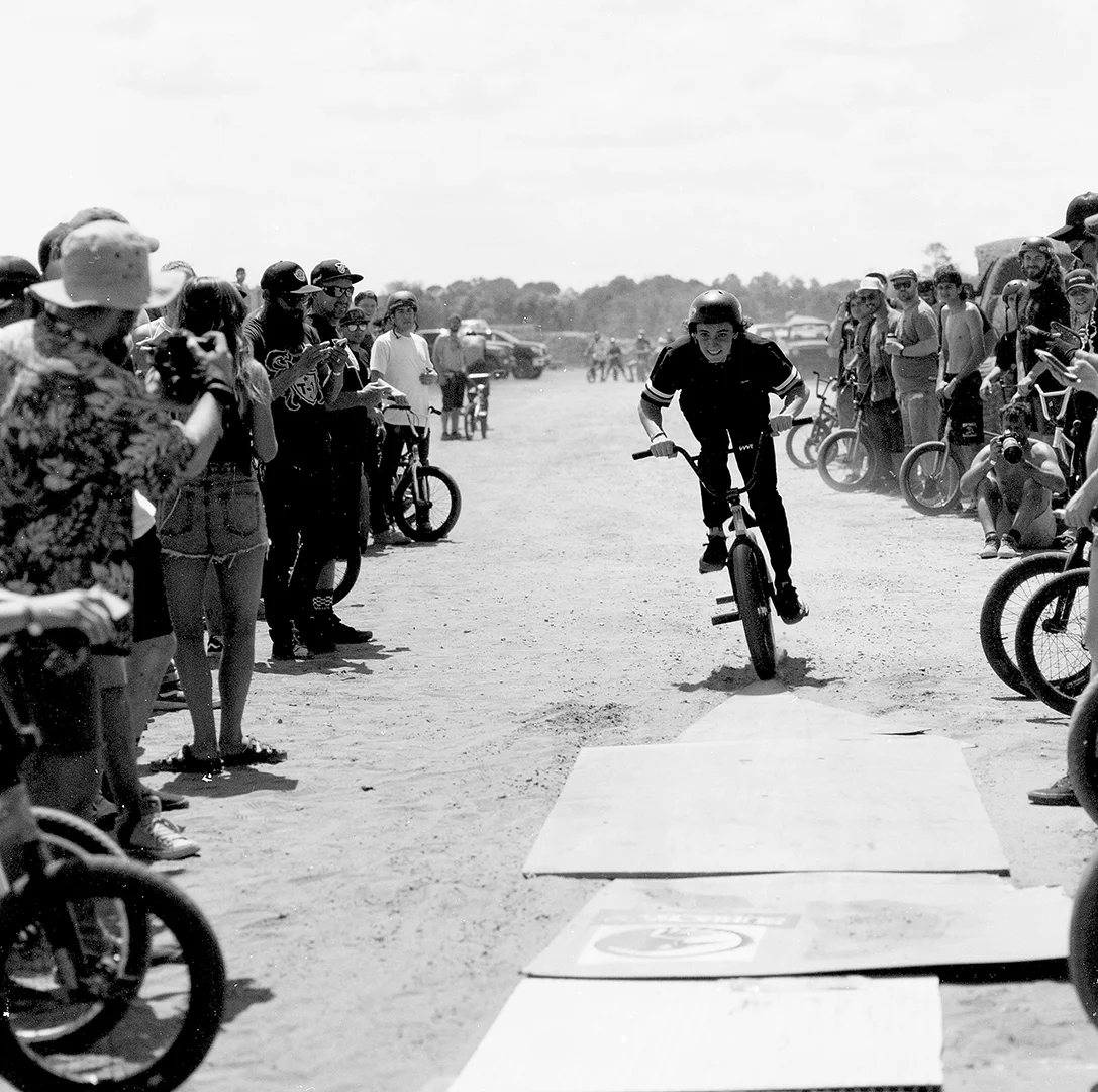 This is Preston Okert. His effortless style on a bike is his secret weapon and the chasm jump at Swampfest was right up his alley, here you see the crowd behind him at the starting point for the jump and this loose scrap wood is the final few feet before taking off the lip. I shot this with a Hasselblad 503cw 150mm F4 on Fomapan 100 film.