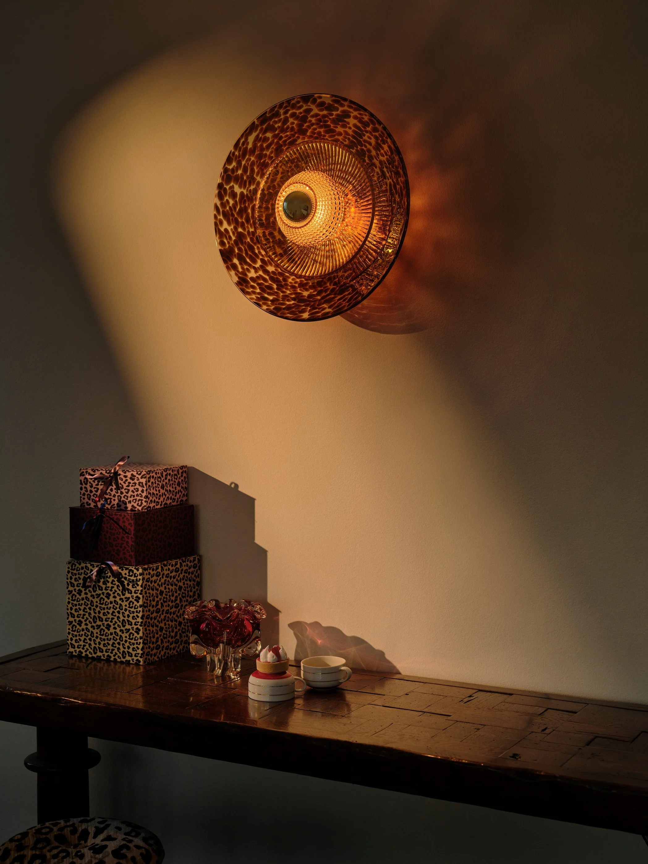 Brown Disco Rama sconce above a wooden console table in a moody interior with leopard-print accessories.
