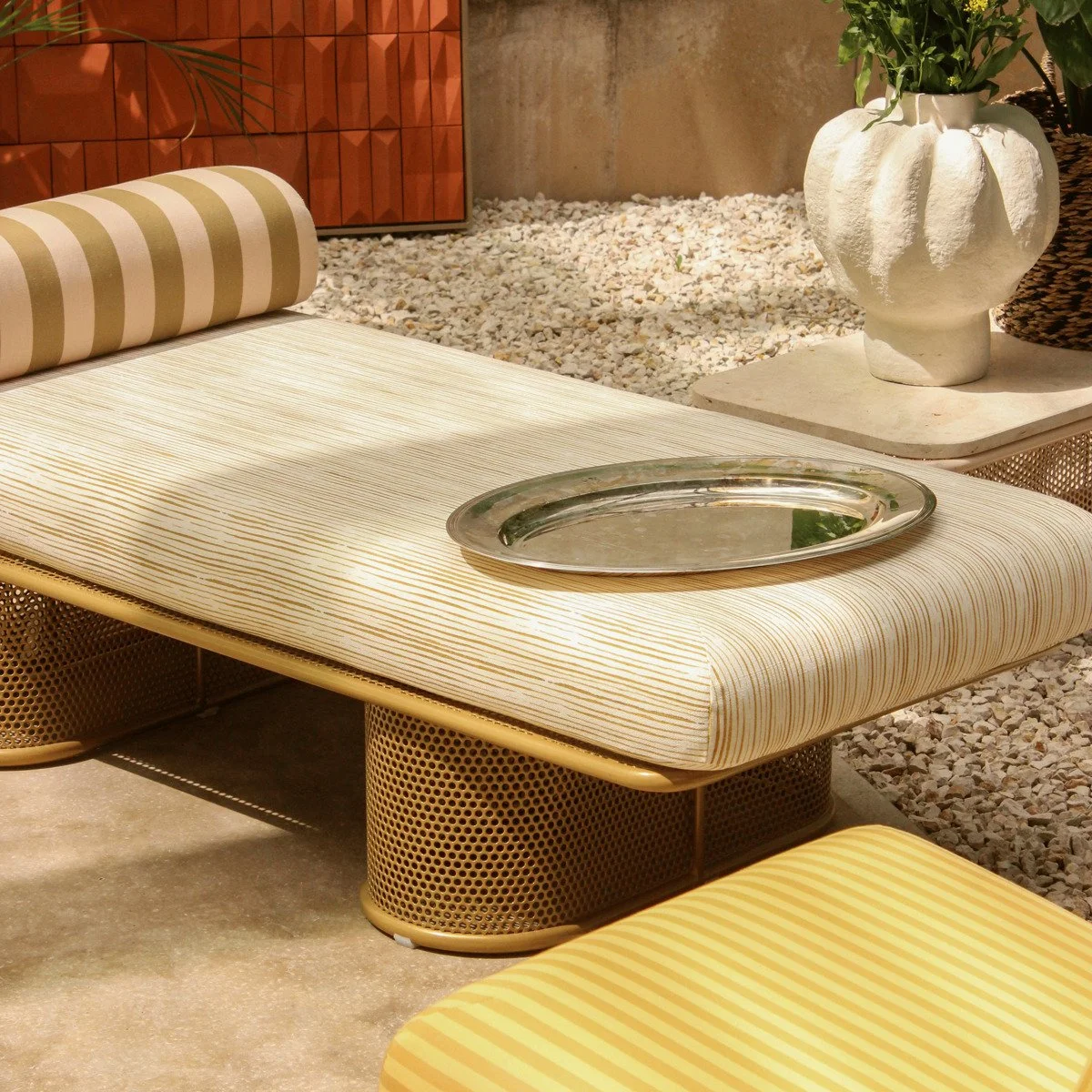 A wide lifestyle shot featuring the Riviera bench and chairs on a gravel-covered courtyard, emphasizing a Mediterranean-inspired outdoor living space.