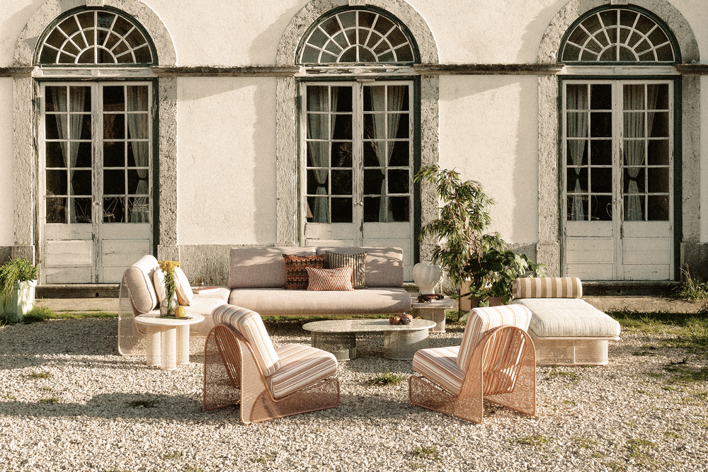 A wide lifestyle shot featuring a curated selection of Riviera outdoor furniture, including an orange metal bench and matching bar stools with striped cushions