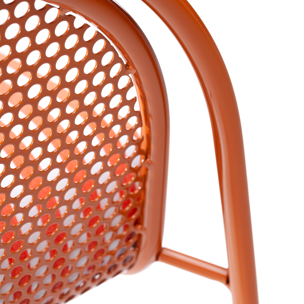 An extreme close-up detail of an orange-coated metal bar chair, focusing on the circular perforated pattern of the backrest and the smooth tubular frame.