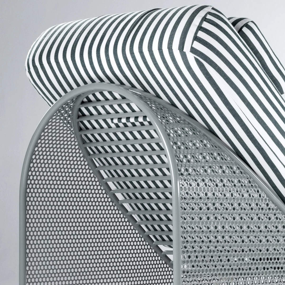 High-angle close-up; grey perforated metal frame detail; focus on the curved structural back and horizontal support slats; striped cushion upholstery.