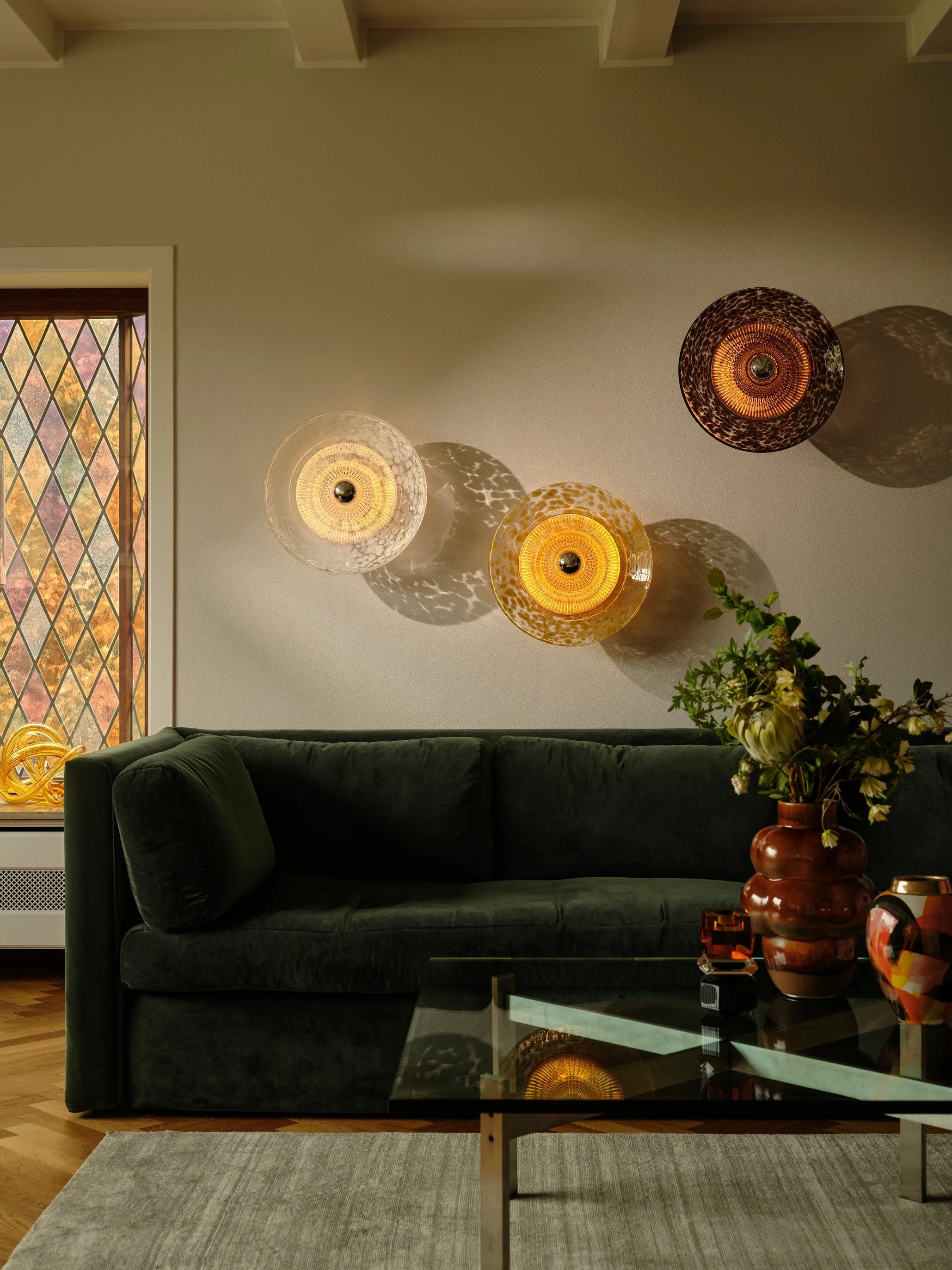 Clear, Amber and Brown Disco Rama sconces grouped above a green velvet sofa in a modern living room.
