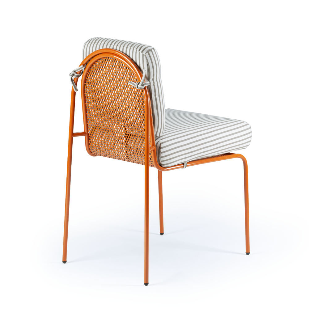 A rear three-quarter view of a Riviera dining chair, highlighting the arched perforated mesh backrest and the striped cushion tie-on details on an orange frame.