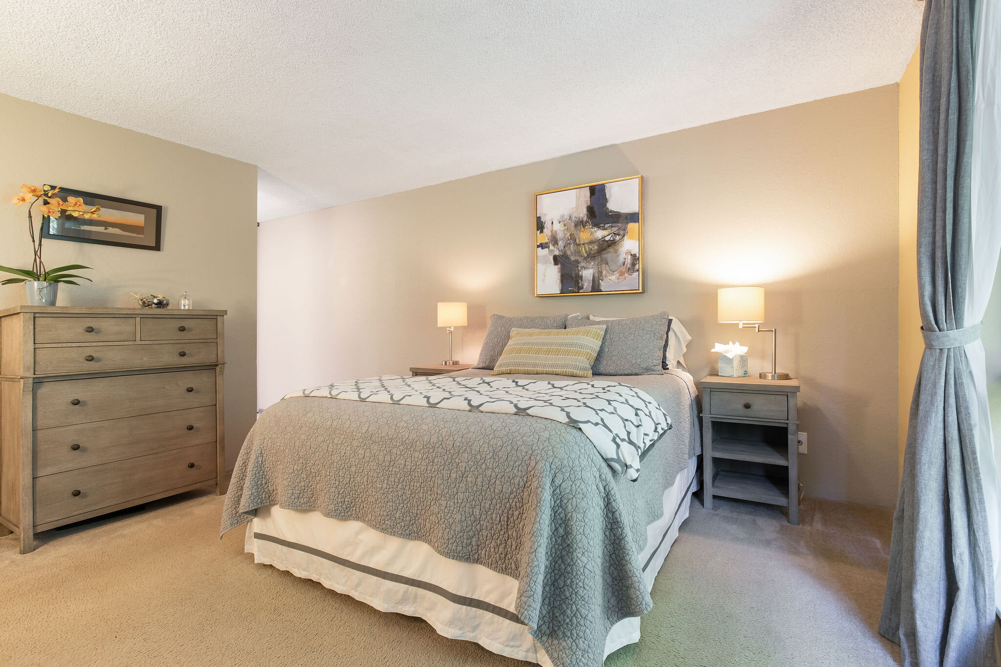  image description: interior of bedroom with queen bed, dresser and large windows 