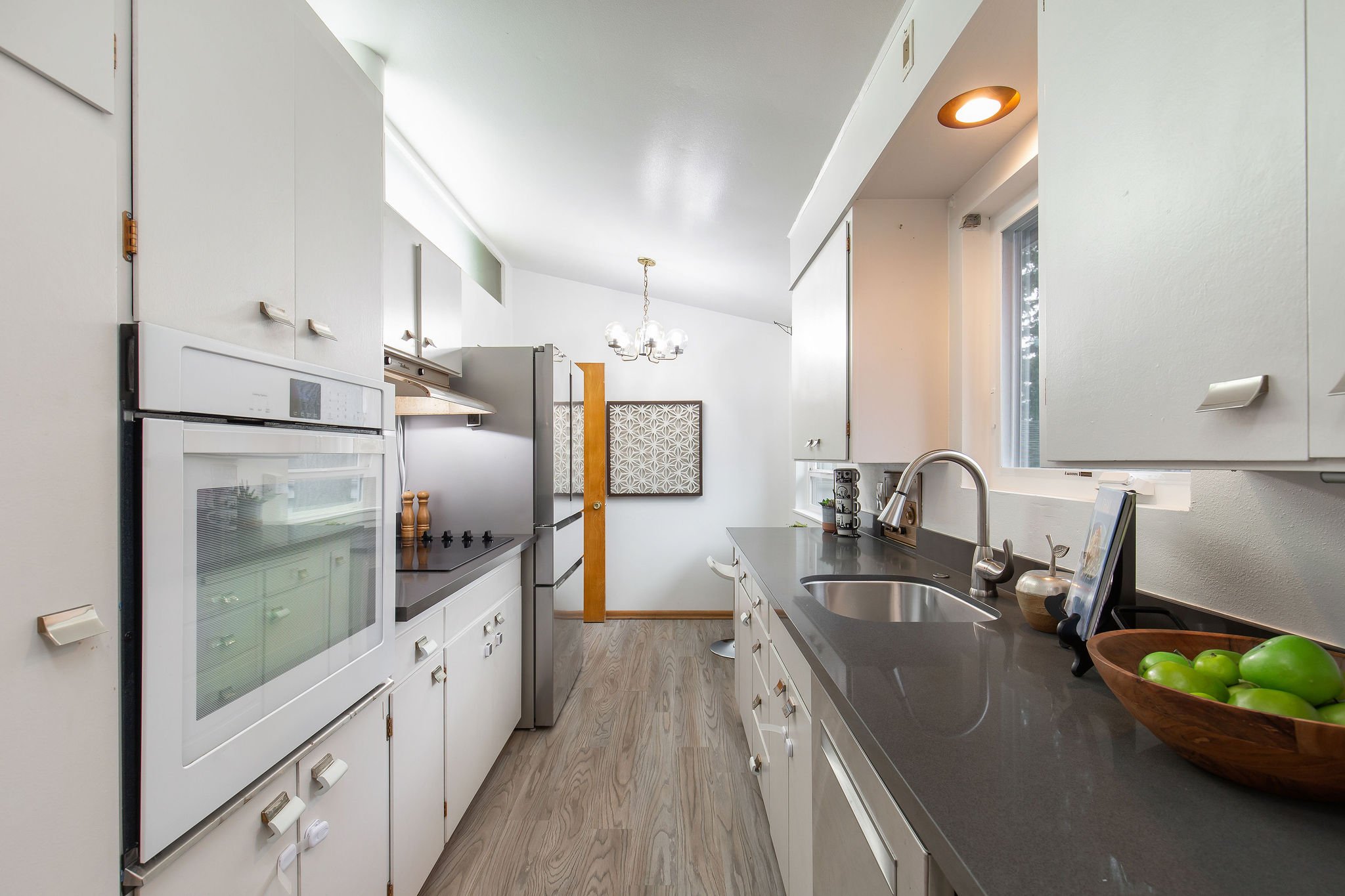  image description: interior of kitchen wit grey countertops, white cabinets, and windows 
