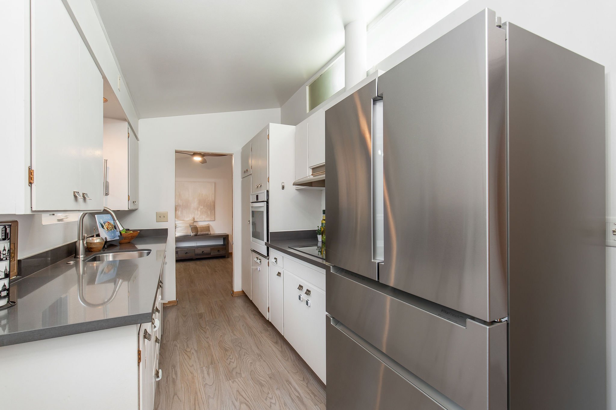  image description: interior of kitchen wit grey countertops, white cabinets, and windows 