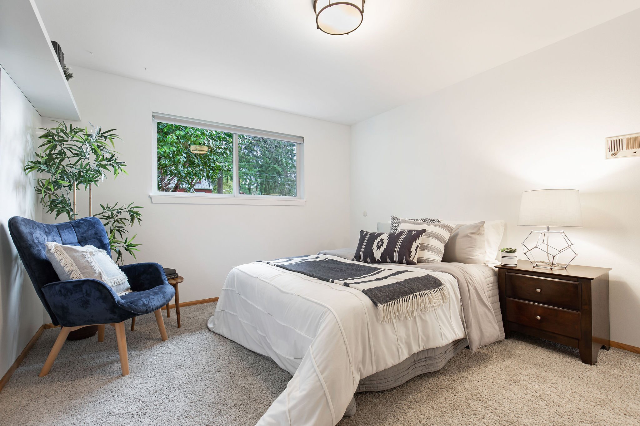  image description: interior of bedroom with queen bed, chair, and window 