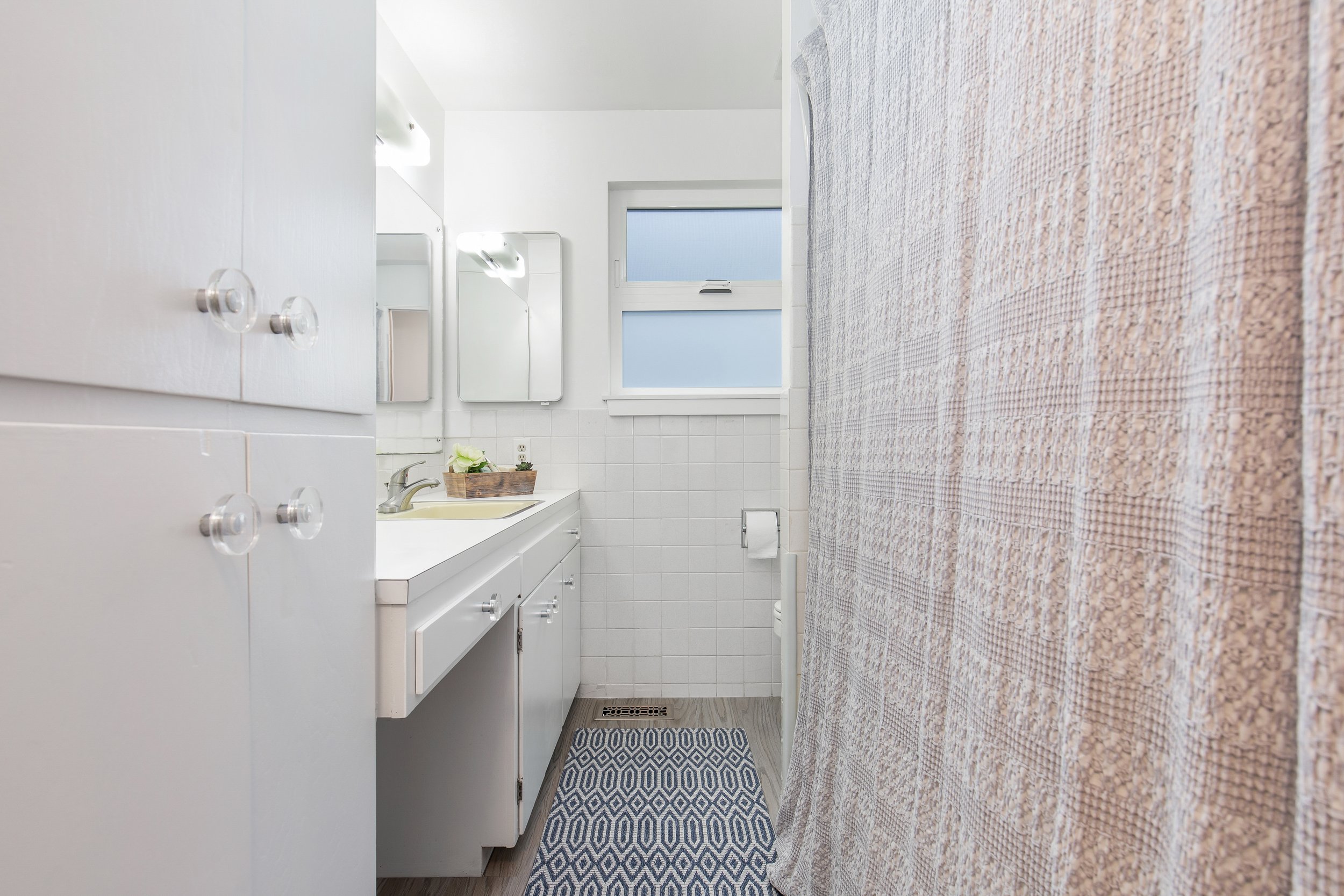  image description: interior of bathroom with window and cabinets 