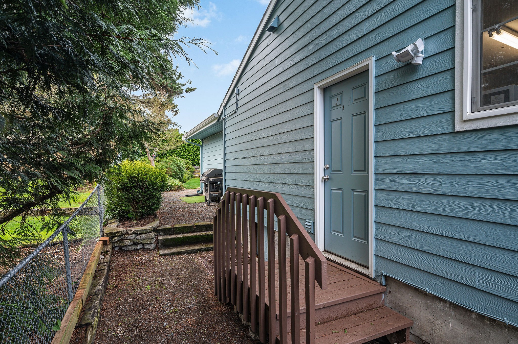  image description: exterior of one story blue house with view of side door and walkway 
