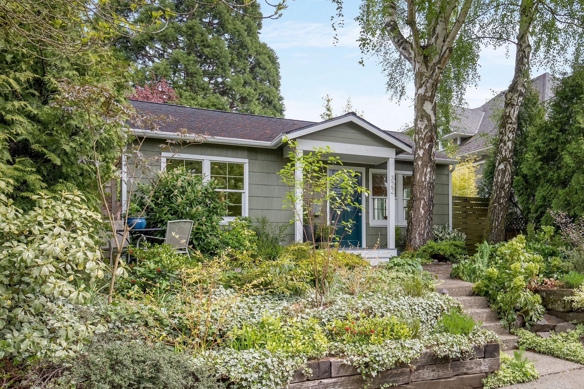  image description: exterior of green one story cottage with garden and yard 