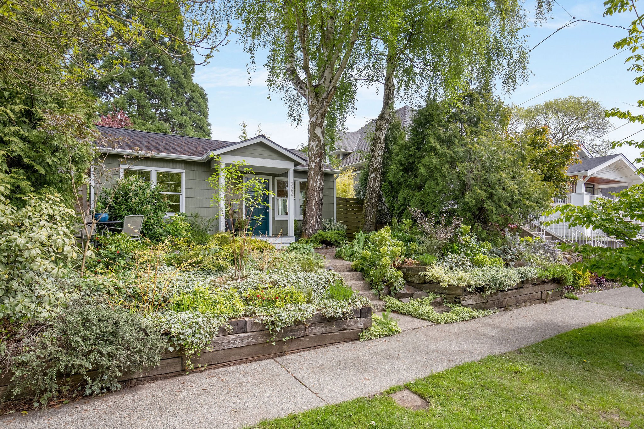  image description: exterior of green one story cottage with garden and yard 