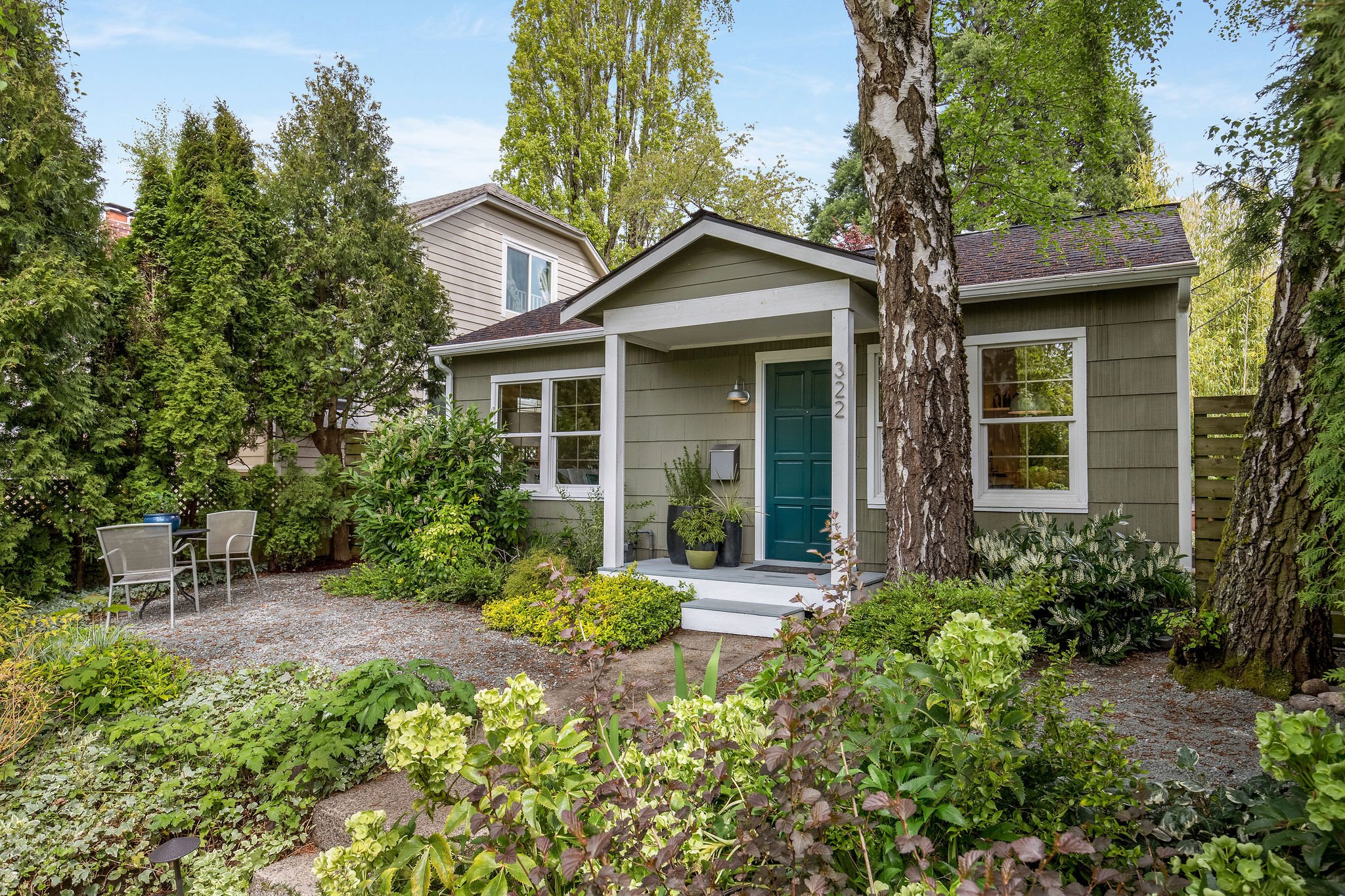  image description: exterior of green one story cottage with garden and yard 