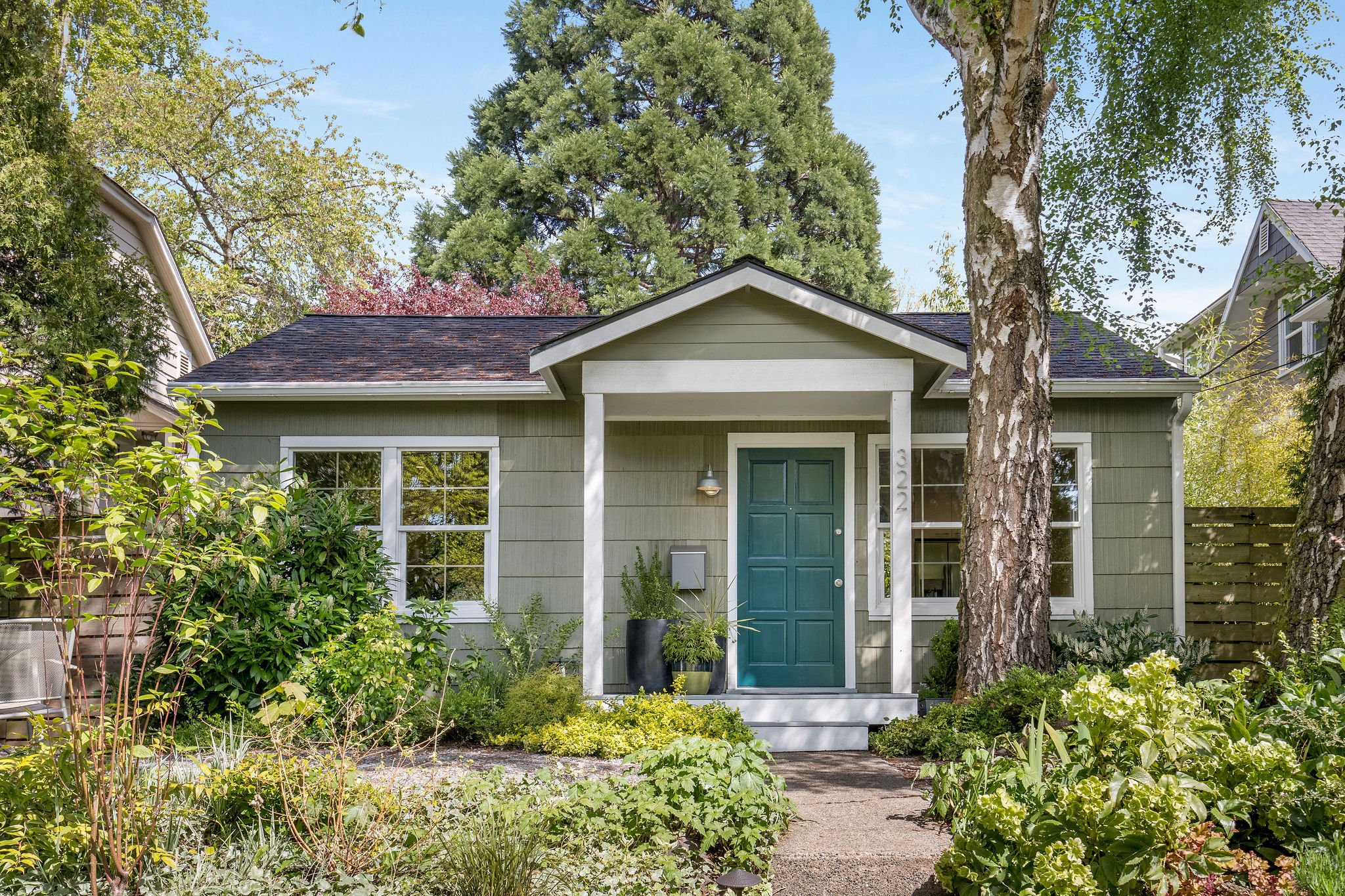  image description: exterior of green one story cottage with garden and yard 