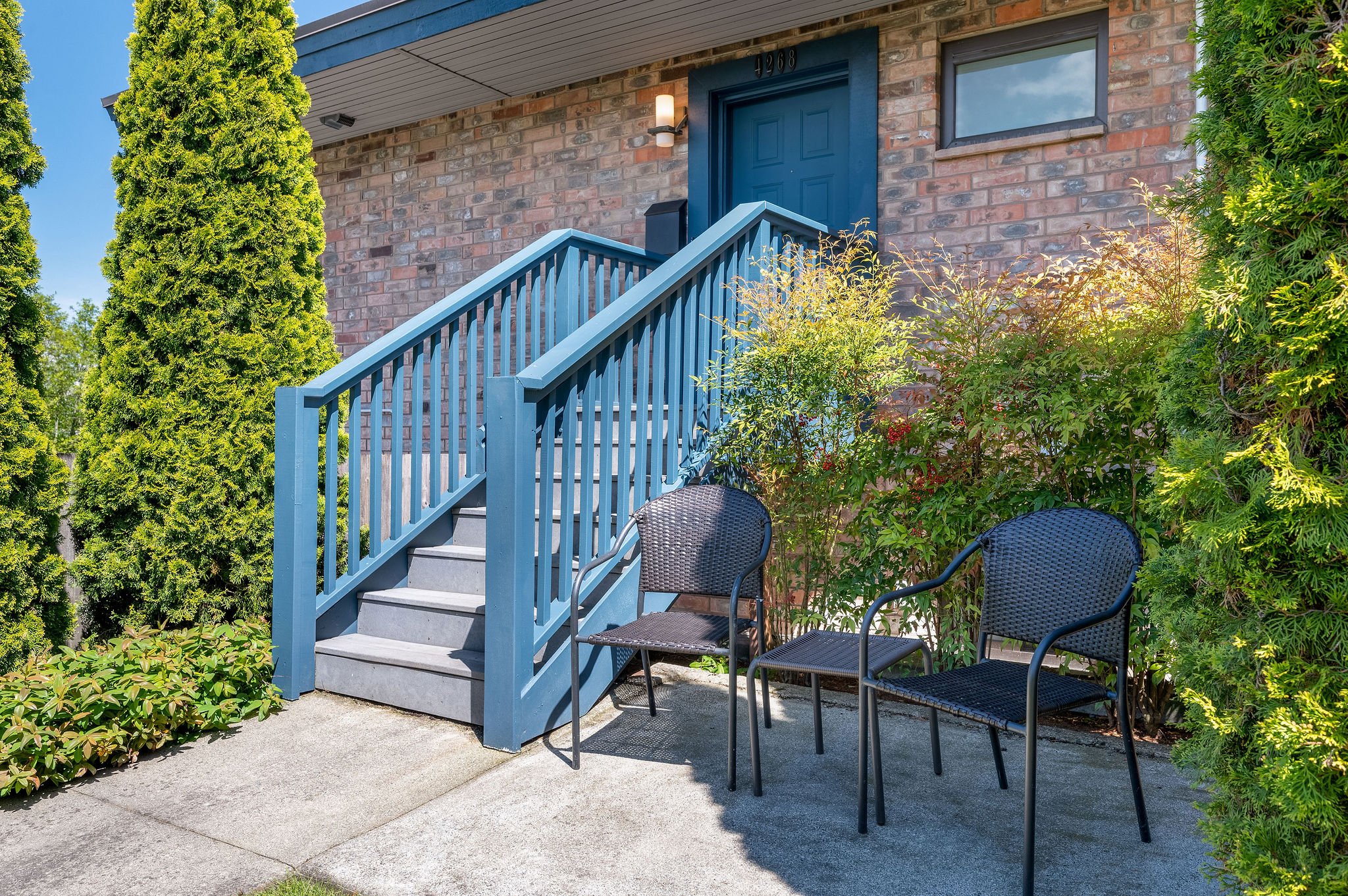  Image description: exterior of condo with stairs, small garden and patio furniture 